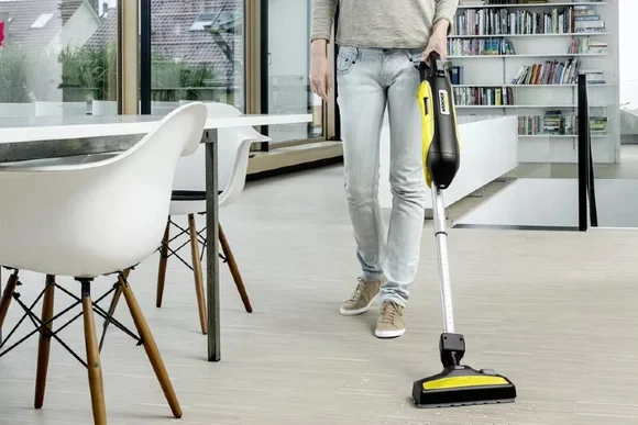 Person saugt Staub mit einem Stabstaubsauger.